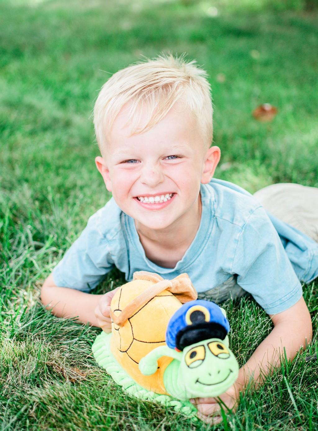 A delighted child hugging his Sunny plush in the grass